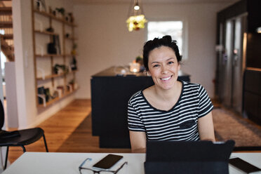 Portrait of smiling mid adult woman using laptop at table in living room - MASF07754