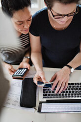 Lesbisches Paar kauft online mit Kreditkarte ein, während sie am Tisch einen Laptop benutzen - MASF07758