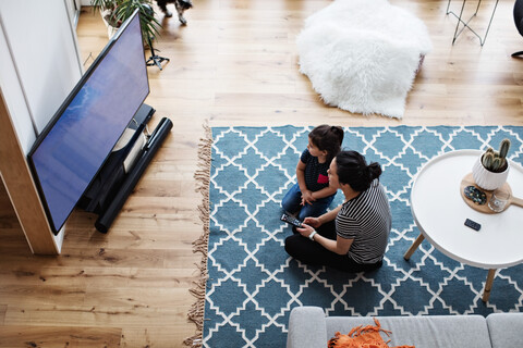 Hochformatige Ansicht von Mutter und Tochter, die zu Hause auf dem Boden sitzend fernsehen, lizenzfreies Stockfoto