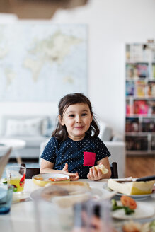 Porträt eines niedlichen lächelnden Mädchens beim Frühstück am Tisch im Haus - MASF07778