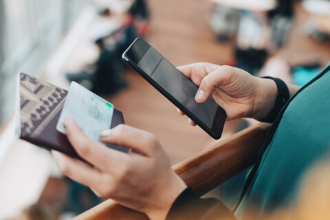 Ausgeschnittenes Bild einer Geschäftsfrau, die eine Kreditkarte hält, während sie ein Mobiltelefon im Flughafen benutzt, lizenzfreies Stockfoto