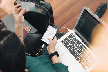 High angle view of businesswoman holding credit card while using mobile phone in airport - MASF07787