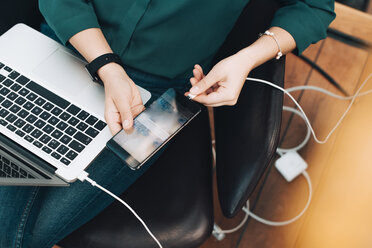 Midsection of businesswoman plugging USB cable into mobile phone at airport - MASF07789