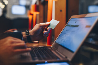 Ausgeschnittenes Bild eines Geschäftsmannes, der eine Kreditkarte hält, während er einen Laptop am Flughafen benutzt - MASF07790