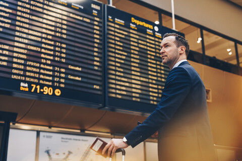 Geschäftsmann schaut auf die Ankunft-Abflug-Tafel im Flughafen, lizenzfreies Stockfoto