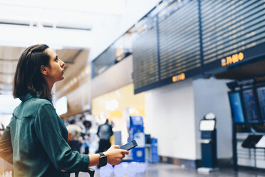 Seitenansicht einer Geschäftsfrau mit Blick auf die Ankunft-Abflug-Tafel im Flughafen - MASF07797