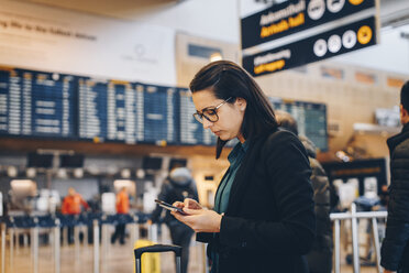 Seitenansicht einer mittleren erwachsenen Geschäftsfrau, die im Flughafenterminal ein Mobiltelefon benutzt - MASF07799
