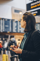 Mittlere erwachsene Geschäftsfrau, die ein Mobiltelefon benutzt, während sie im Flughafen steht - MASF07801