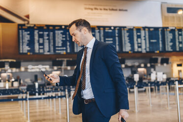 Mature businessman using mobile phone while walking in airport terminal - MASF07804