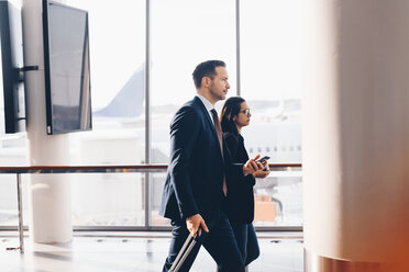 Side view of businessman and businesswoman walking in airport terminal - MASF07810