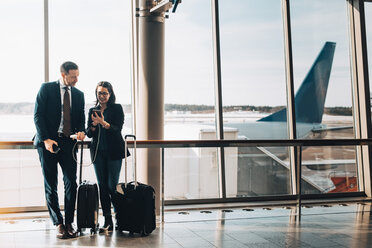 Full length of business couple with luggage using mobile phone in airport - MASF07819