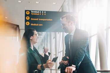 Smiling business couple holding mobile phones white talking in airport - MASF07820