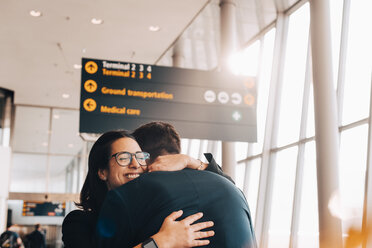 Lächelnde Geschäftsfrau umarmt Geschäftsmann im Flughafenterminal - MASF07824