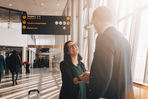 Lächelnde Geschäftsfrau beim Händeschütteln mit Geschäftsmann im Flughafenterminal - MASF07827