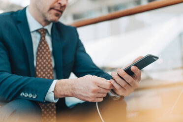 Midsection of businessman plugging USB cable into mobile phone at airport - MASF07835