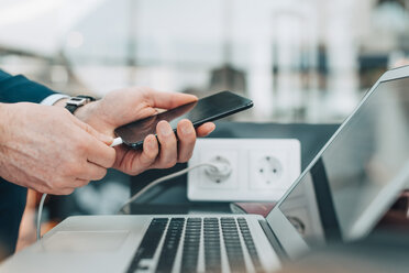 Cropped image of businessman plugging USB cable into smart phone at airport - MASF07836