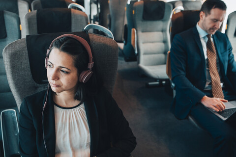 Businesswoman using headphones while traveling with businessman in train stock photo