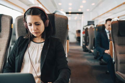 Mid adult businesswoman using headphones and laptop while traveling in train stock photo
