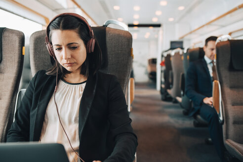 Mittlere erwachsene Geschäftsfrau mit Kopfhörern und Laptop während der Fahrt im Zug - MASF07856