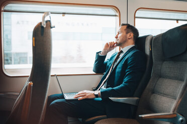 Thoughtful businessman with laptop traveling in train - MASF07857