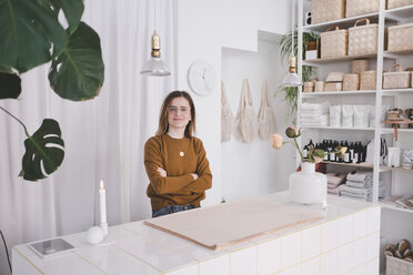 Portrait of young female entrepreneur standing arms crossed at desk in studio - MASF07864