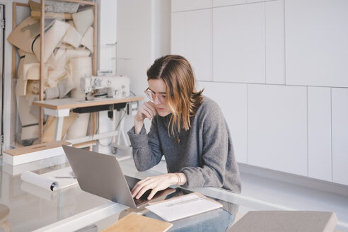 Junge Modedesignerin mit Laptop am Schreibtisch in einem Geschäft - MASF07886