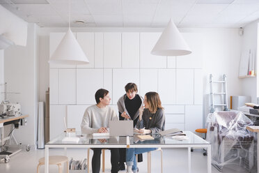 Modedesignerinnen diskutieren am Schreibtisch im Atelier über einen Laptop - MASF07891