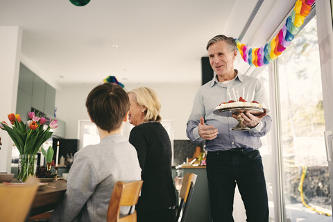 Junge sieht Großvater an, der Geburtstagskuchen auf einer Party hält, lizenzfreies Stockfoto