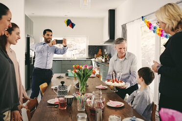 Mann fotografiert Junge mit Familie während Geburtstagsfeier mit Smartphone - MASF07932