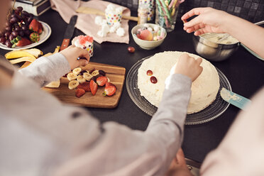 Ausgeschnittenes Bild von Geschwistern, die am Küchentisch Kuchen verzieren - MASF07940