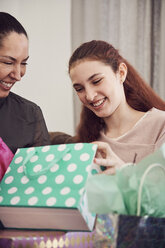 Excited girl looking at birthday present while sitting with mother at home - MASF07943