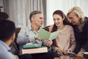 Grandfather reading greeting card to happy family while sitting on sofa at home - MASF07945