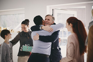 Smiling senior father embracing man while standing by family at doorway - MASF07947