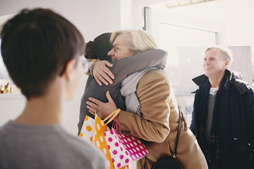 Ältere Frau, die ihre Tochter umarmt, während sie mit ihrer Familie vor der Tür steht - MASF07951