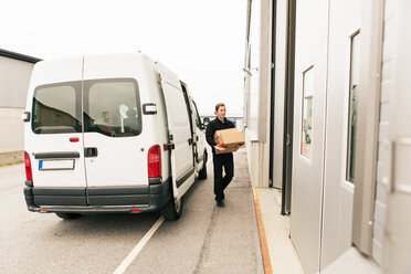 Arbeiter in voller Länge, der Kartons trägt, während er an einem Lieferwagen vorbeigeht - MASF07964