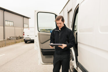 Handwerker, der ein digitales Tablet am Lieferwagen benutzt, während er auf der Straße steht - MASF07971