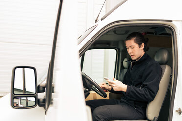 Side view of manual worker using mobile phone while sitting in delivery van - MASF07973