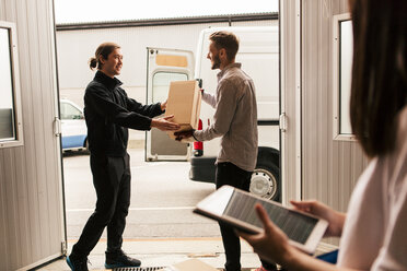 Eine Frau benutzt ein digitales Tablet, während männliche Mitarbeiter Kisten in einem Lieferwagen ausliefern - MASF07974