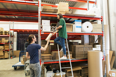 Frau gibt aufgerollten Karton an männlichen Mitarbeiter in der Industrie in voller Länge, lizenzfreies Stockfoto