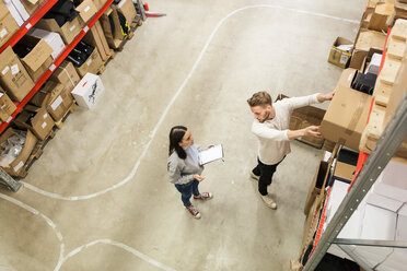 Colleagues discussing while examining cardboard boxes in industry - MASF07989