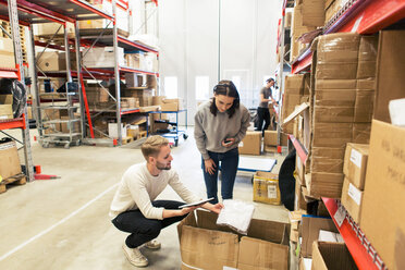 Coworkers examining manufactured objects while using digital tablet at warehouse - MASF08002