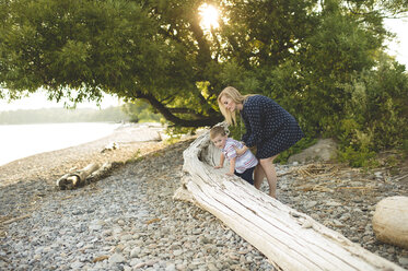 Boy with mother climbing onto tree trunk at Lake Ontario, Oshawa, Canada - CUF20914