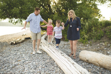 Mid adult parents holding hands with boy and girl on tree trunk at Lake Ontario, Oshawa, Canada - CUF20915