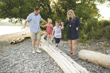 Mittlere erwachsene Eltern halten sich mit einem Jungen und einem Mädchen auf einem Baumstamm am Ontariosee, Oshawa, Kanada, an den Händen - CUF20915