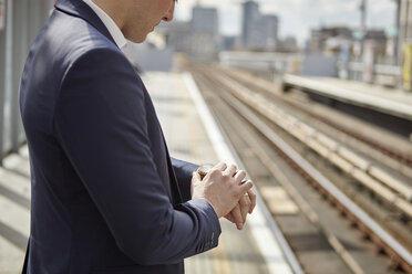 Cropped shot of businessman checking watch at train platform, London, UK - CUF20974