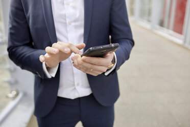 Mittelteil eines Geschäftsmannes auf einer Fußgängerbrücke, der eine SMS auf seinem Smartphone schreibt, London, UK - CUF20975