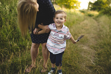 Mother bending down to son with handful of feathers in meadow - CUF20980