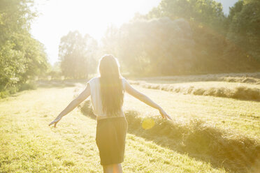 Rear sunlit view of young woman with arms open in field, Vogogna,Verbania,Piemonte, Italy - CUF20983