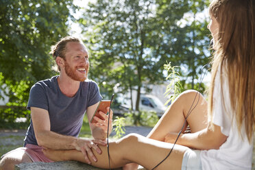 Young couple outdoors, listening to music through earphones - CUF20991