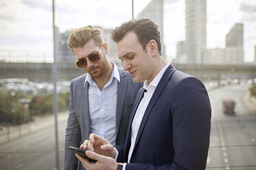 Zwei Geschäftsleute auf einer Fußgängerbrücke schreiben eine SMS mit ihrem Smartphone, London, UK - CUF21006